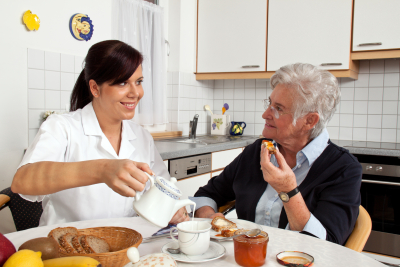 A geriatric nurse helping senior at breakfast